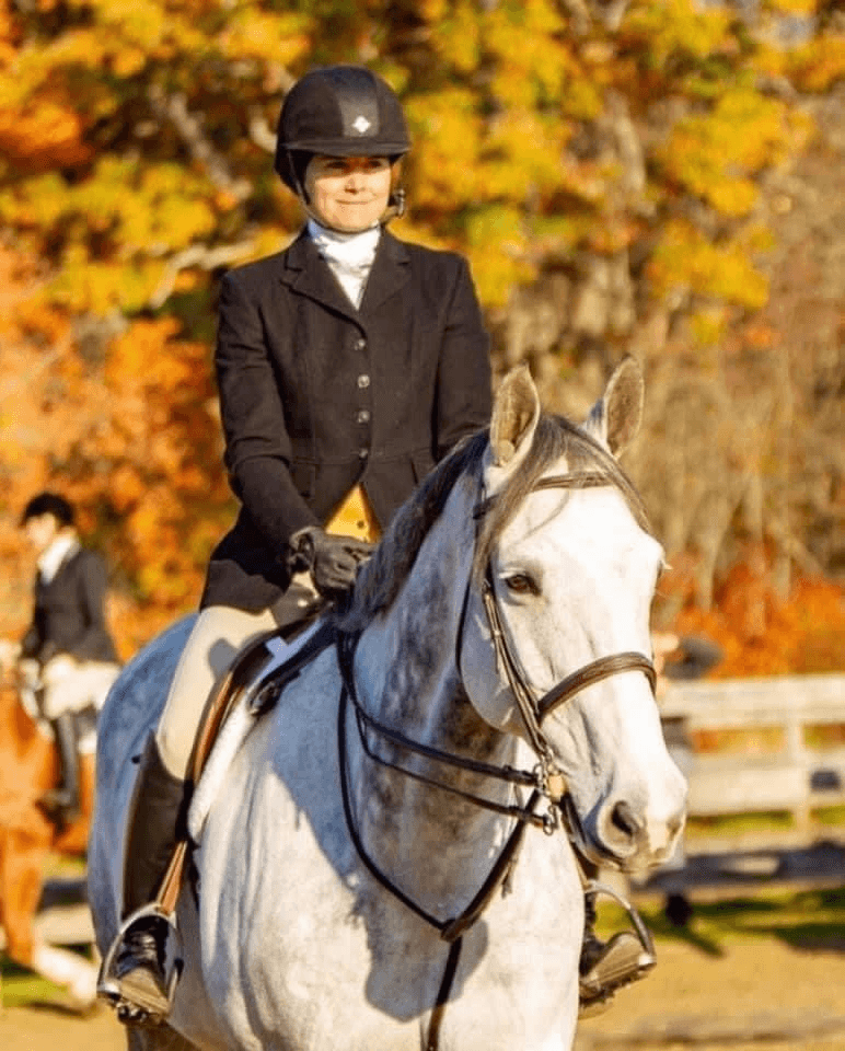 Womam in black coat on grey horse.