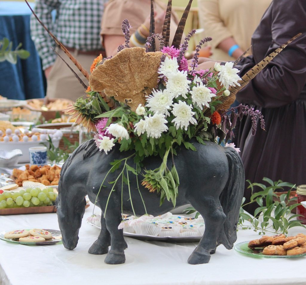 Horse statue with flower arrangement next to food on table.